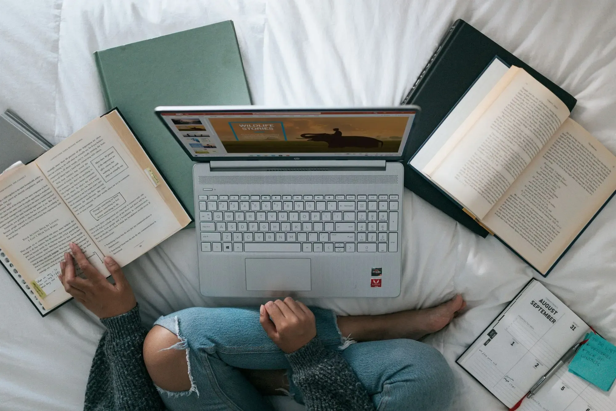 person sitting on bed with a laptop and books